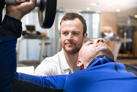 Trainer beobachtet Gast beim Gewichte stämmen