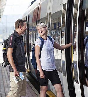 Mann und Frau steigen im Wanderoutfit in den Zug