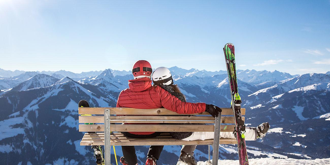 Skifahrer-Pärchen genießt den Ausblick auf einer Bank
