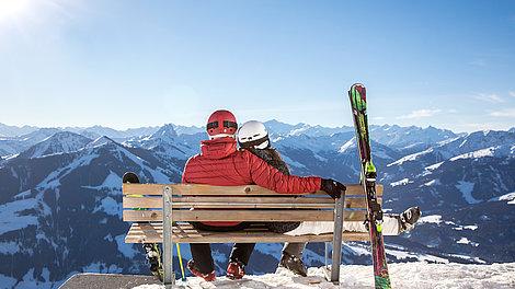 Skiing couple enjoys the view from a bench