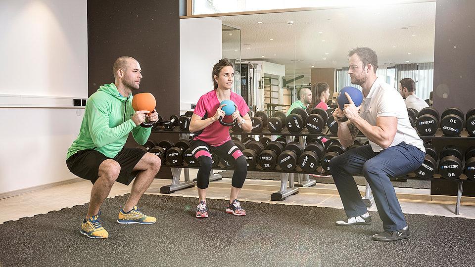 Trainer zeigt Gästen eine Fitnessübung mit Ball
